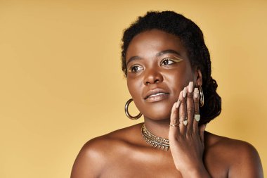 Genç siyah bir kadın parlak tenini parlak sarı bir arka planda sergiliyor..