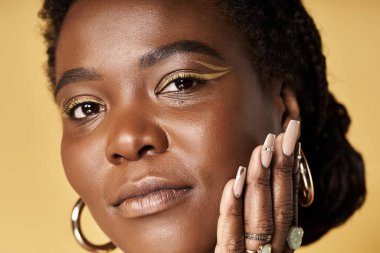 Genç Afrikalı Amerikalı kadın stüdyo ortamında parlak bir ten ve eşsiz bir makyaj sergiliyor..