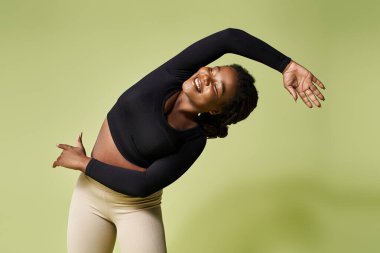 Genç bir Afrikalı Amerikalı kadın neşeli bir şekilde parlak bir stüdyoda esniyor, güç ve zarafeti somutlaştırıyor..