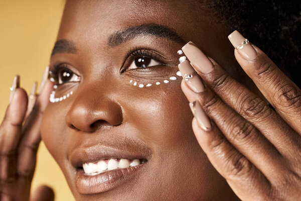 A young African American woman enhances her beauty with intricate designs under her eyes.