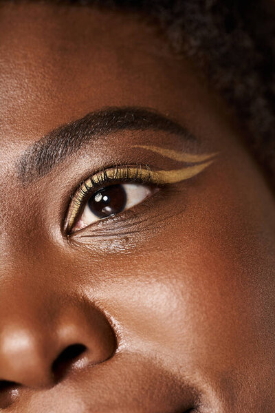 Young woman showcases radiant skin and bold eyeliner in a creatively lit studio setting.