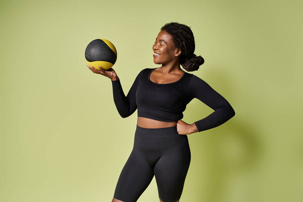 A young, fit African American athlete smiles while balancing a workout ball.