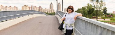 Güzel bir kadın modern şehir binaları ve afişlerle çevrili manzaralı bir köprüde egzersiz yapıyor.