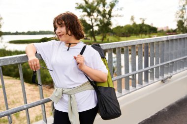 Formda bir kadın nehir kenarında egzersiz yapıyor. Açık hava egzersizlerini ve özgüvenini sergiliyor..