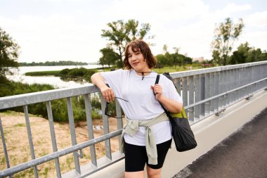 Güzel bir açık havada egzersiz yapmaya hazır, sağlıklı genç bir kadın köprüde duruyor..