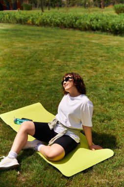 Formda bir kadın, doğadaki antrenmanından sonra güneşi emerek paspasın üzerinde dinlenir..