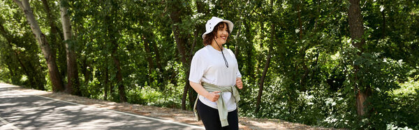 Smiling woman in activewear jogs along a peaceful path surrounded by lush trees, banner