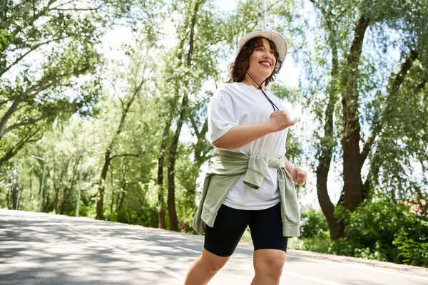 Gün ışığı ağaçların arasından parlıyor. Genç bir kadın manzaralı, doğa dolu bir yolda koşarken..
