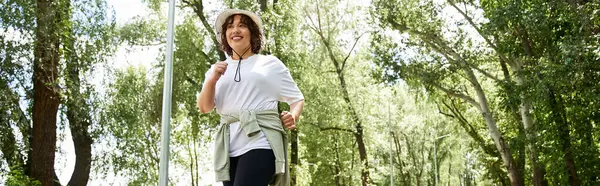 Zinde ve aktif bir kadın gündüz vakti yemyeşil bir yolda neşeyle koşar.