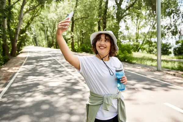 Neşeli genç bir kadın doğa ile çevrili dışarıda çalışırken selfie çekiyor..