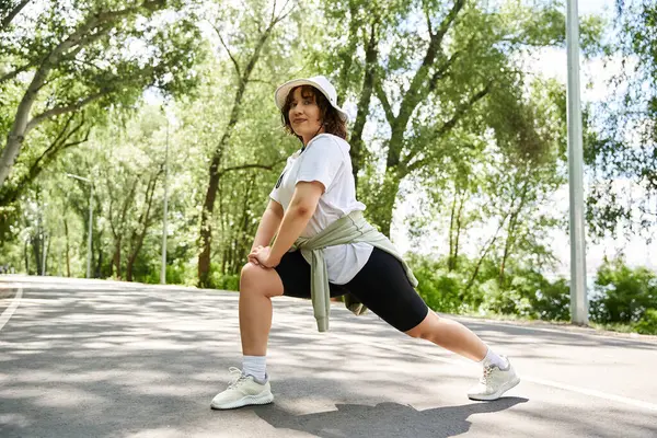 Genç bir kadın esneme hareketlerini ağaçlarla çevrili sakin bir açık havada yapıyor..