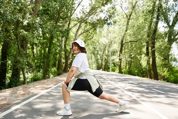 Zinde bir kadın egzersiz yaparken yemyeşil bir alanda sakin bir yol boyunca uzanır..