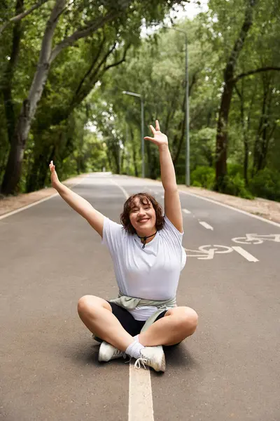 Genç bir kadın sakin bir yolda rahatlıyor, gülümsüyor ve yaz havasını kucaklıyor..