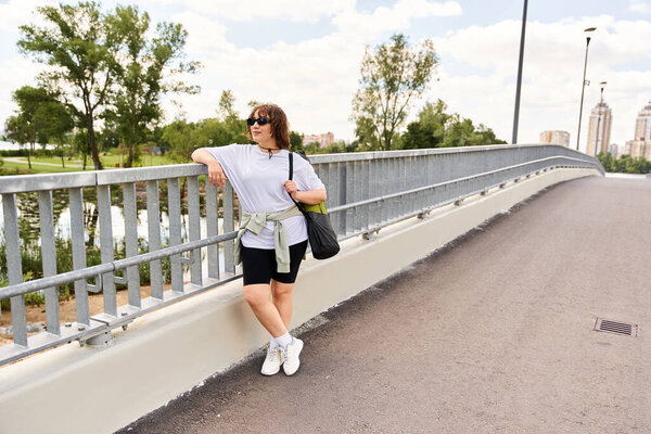 A pretty young woman relaxes after a workout outdoors by the river, soaking in the urban landscape.