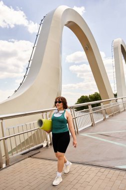 Güzel bir kadın, dışarıda egzersiz yaparken yoga minderi taşıyarak rahatça yürür..