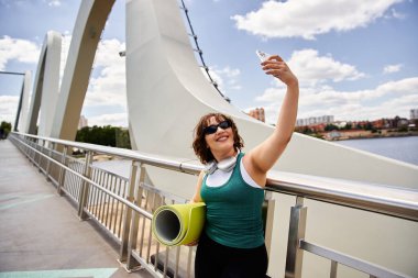 Genç bir kadın dışarıda çalışmaktan zevk alıyor, akıllı telefonuyla neşeli bir anı yakalıyor..