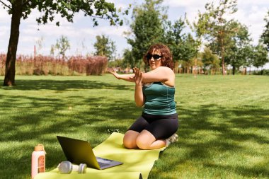 Genç bir kadın açık bir gökyüzünün altındaki çimenli bir arazide kolunu uzatıyor ve internetteki fitness 'i destekliyor.