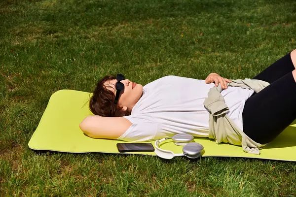 Genç bir kadın açık havada eğlenirken yaz güneşini emerek yeşil bir mindere uzanır..