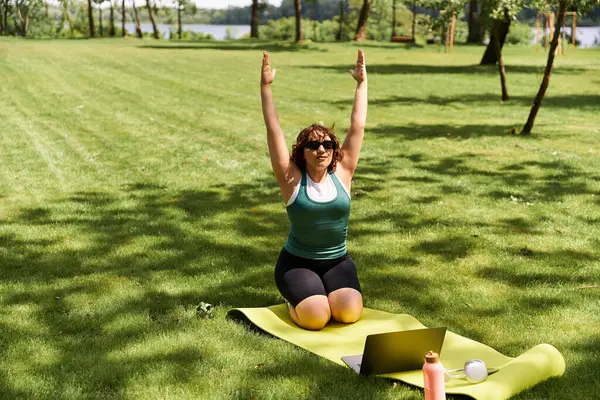 Güzel, genç bir kadın yemyeşil bir parkta egzersiz yapıyor. Formuna ve sağlığına odaklanıyor. İnternet üzerinden egzersiz yapıyor.