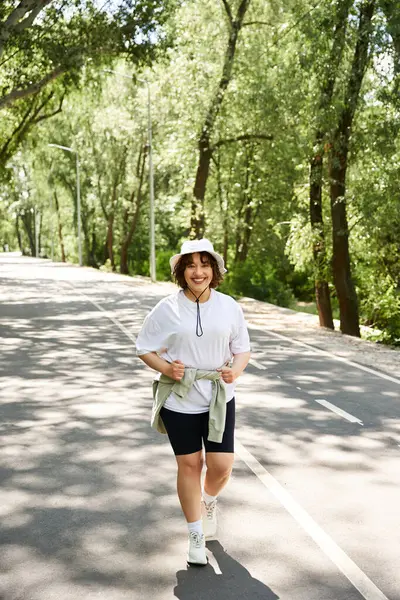 Genç bir kadın, yemyeşil ve güneş ışığıyla çevrili açık havada mutlu bir şekilde egzersiz yapıyor..