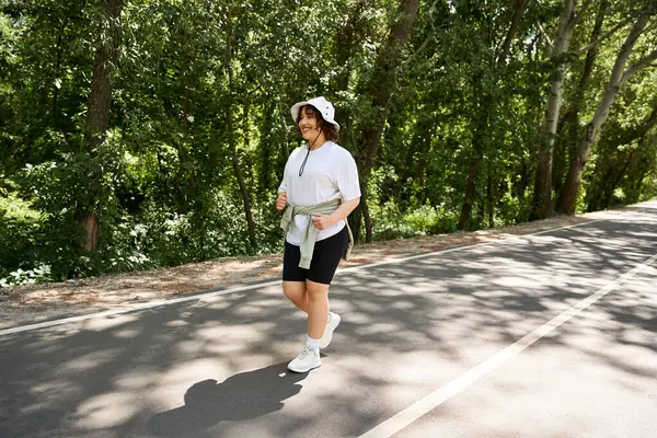 Genç bir kadın ağaçlık bir yolda mutlu bir şekilde koşuyor, doğadaki spor rutininin tadını çıkarıyor..