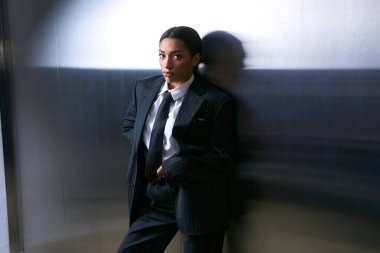 Özel dikim takım elbiseli şık bir kadın metalik bir arka plana karşı duruyor, zarafet saçıyor..