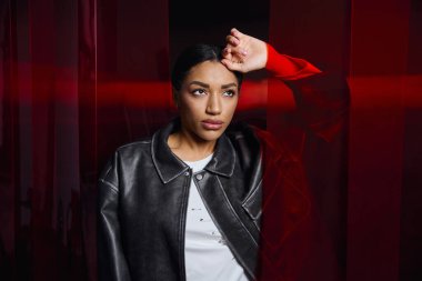 Şık genç kadın kendine güvenerek poz veriyor, zarafetle modern modayı çarpıcı bir ışıkla karıştırıyor..