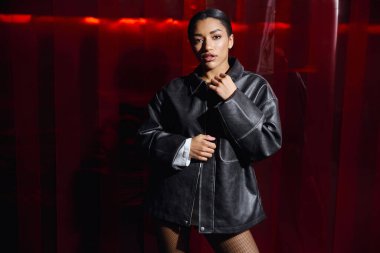 Tarz sahibi genç bir kadın çarpıcı bir arka plana karşı kendine güvenen bir şekilde poz veriyor..