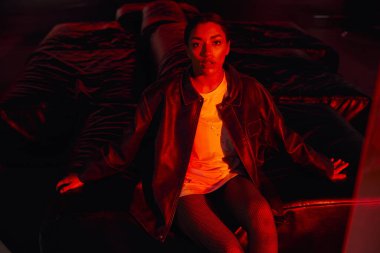 Şık, genç bir kadın rahat bir şekilde oturarak, sıcak kırmızı ışıkla aydınlanır..