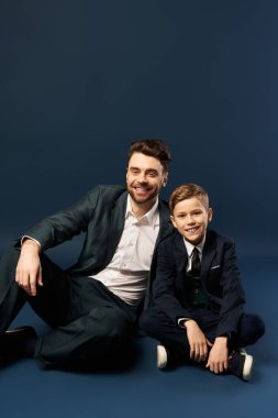 Bir baba ve oğul, şık giyinmiş bir şekilde gülümseyerek beraberlik anını yakalar..