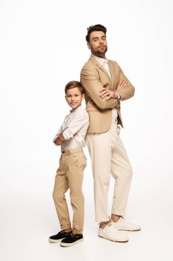 Bir baba ve oğul gururla sırt sırta durur şık kıyafetleriyle, neşe saçar.