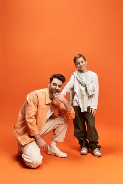 Bir baba oğlunun yanında gülümseyerek diz çöker, beraberlik ve kutlama ruhunu kucaklar..