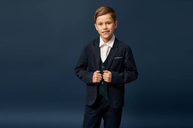 Şık takım elbiseli neşeli bir çocuk, karanlık zeminde poz veriyor..