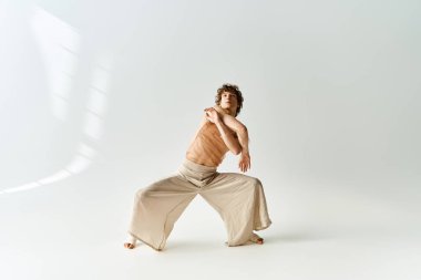 Genç, kıvırcık bir adam gri bir stüdyoda dinamik dans yeteneklerini sergiliyor..