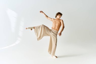 Kıvırcık saçlı genç bir adam gri bir stüdyoda dans ederken atletik yeteneklerini sergiliyor..