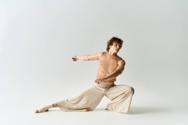 Kıvırcık saçlı genç adam bir stüdyoda zarif bir şekilde dans ediyor. Tarafsız bir arka planı var..