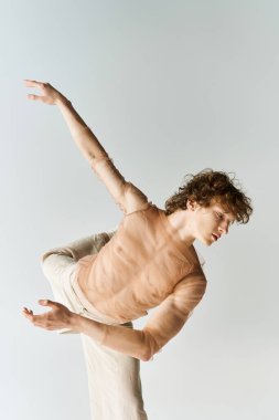 Kıvırcık saçlı genç bir adam gri bir stüdyoda enerjik bir şekilde dans ediyor..