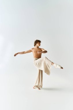 Kıvırcık saçlı genç bir adam stüdyoda zarif bir şekilde dans ediyor, atletizm ve sanatçılık sergiliyor..