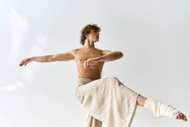 Kıvırcık saçlı genç bir adam, minimalist bir stüdyoda zarif bir şekilde dans ediyor..