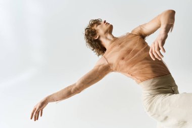 Genç bir adam açık gri bir stüdyoda zerafetle dans ediyor, yeteneğini ve atletizmini sergiliyor..