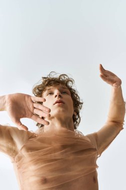 Kıvırcık saçlı dansçı gri bir arka plana karşı zarafetle performans sergiliyor, atletizm ve enerji saçıyor..