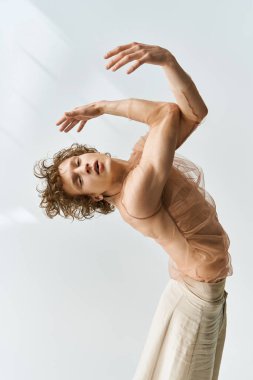 Kıvırcık saçlı genç bir adam, atletizmini dans hareketleriyle bir stüdyoda sergiliyor..