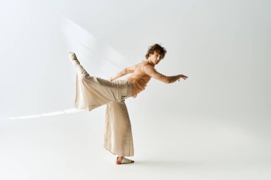 Genç, kıvırcık bir adam dans için tutkusunu ifade eder, gri bir stüdyoda akıcı bir şekilde hareket eder..