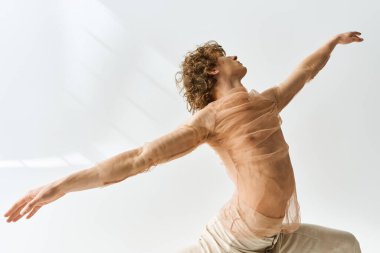 Genç, kıvırcık bir adam dans yeteneklerini sergiliyor. İyi aydınlatılmış bir stüdyoda. Gri bir arka planı var..