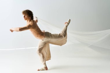 Kıvırcık saçlı genç bir adam gri arka planda zarif bir şekilde dans ediyor, atletizmini sergiliyor..