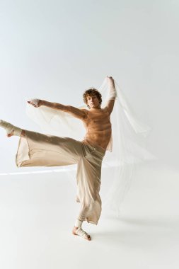 Kıvırcık saçlı genç bir adam stüdyoda zarif bir şekilde dans ediyor, atletizm ve sanatçılık yayıyor..