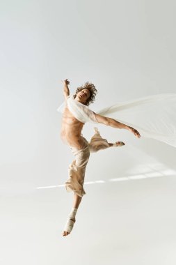 Kıvırcık saçlı genç bir adam minimalist bir stüdyoda dans ederken atletizmini sergiliyor..