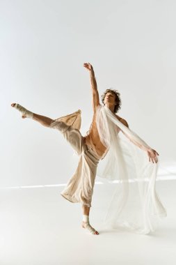 Kıvırcık genç adam sakin bir stüdyo ortamında zarif bir şekilde dans ederken atletizmini sergiliyor..