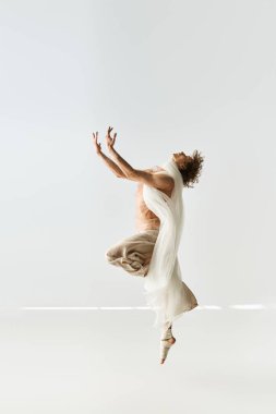 Genç, kıvırcık bir adam canlı dansını minimalist gri bir zemine karşı sergiliyor..