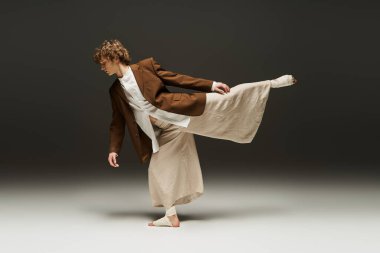 Genç, kıvırcık bir adam stüdyo ortamında zarif bir şekilde dans ederek yeteneğini sergiliyor..